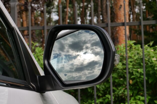 Foto der bewölkte himmel spiegelt sich im spiegel eines in der nähe des eisenzauns geparkten autos wider