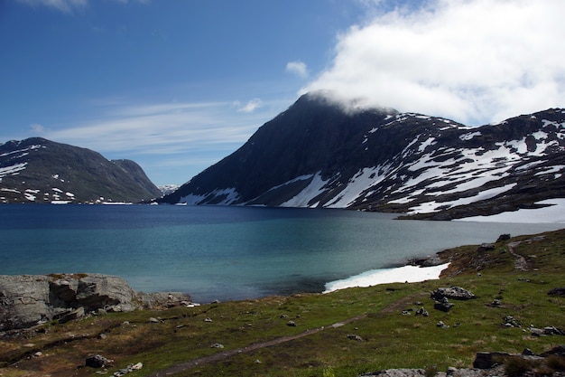 Der blaue See liegt am Fuße der schneebedeckten Berge im Sommer in Norwegen