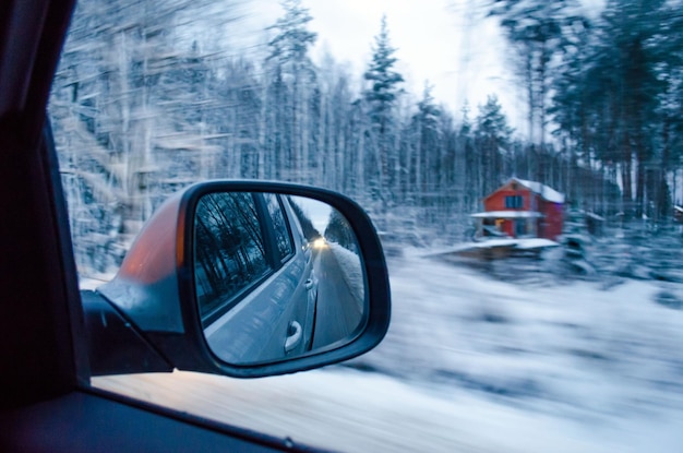 Der Blick aus dem Fenster des Autos auf den Rückspiegel und den schneebedeckten Wald