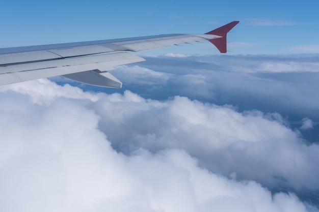 Der Blick aus dem Fenster des Flugzeugs auf den Flügel des Flugzeugs vor dem Hintergrund von flauschigen, lockigen Wolken und blauem Himmel