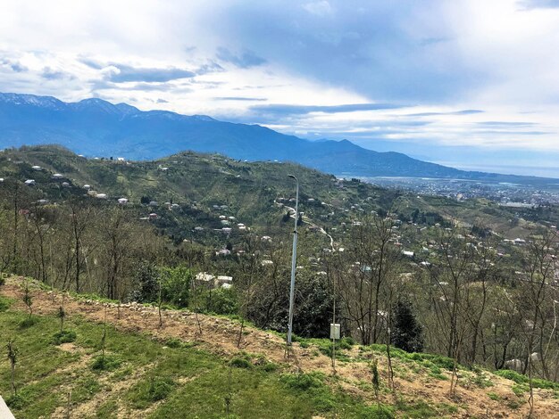 Der Blick von oben aus einer Höhe einer schönen touristischen Stadt mit Gebäuden und Häusern Dächern von Bäumen und Pflanzen Natur gegen einen blauen Himmel und Berge Europäische alte Architektur