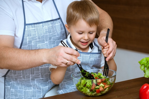 Der blonde Sohn und der blonde Vater bereiten einen Salat aus buntem frischem Gemüse zu