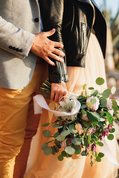 Der Bräutigam hält die Hand der Braut mit einem Blumenstrauß