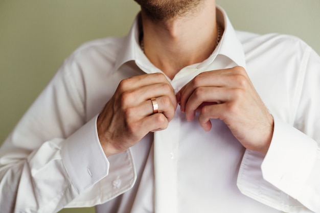 Der Bräutigam in einem weißen Hemd befestigt die Knöpfe. Nahaufnahme des Bräutigammeetings.