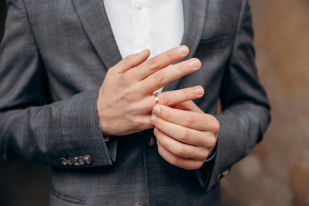 Der Bräutigam in grauer Jacke und roter Fliege legt seinen Ehering an seinen Finger Hochzeitszeremonie Nahaufnahmefoto der Hände eines Mannes mit einem Ehering