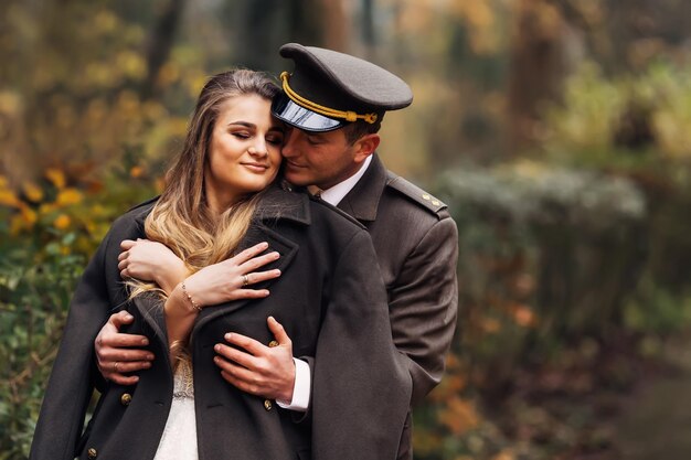 Der Bräutigam in Militäruniform umarmt die Braut im Hochzeitskleid