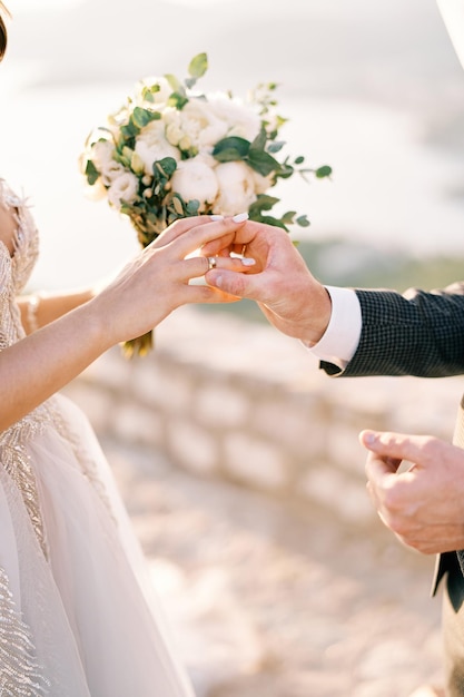 Der Bräutigam setzt einen Ring auf den Finger der Braut mit einem Blumenstrauß, der gesichtslos geschnitten ist.