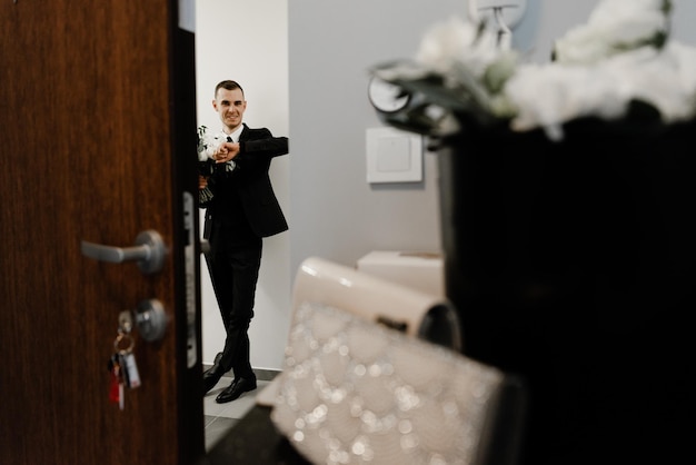Der Bräutigam wartet auf die Braut, die unter der Tür steht und einen Hochzeitsstrauß aus Rosen in der Hand hält. Versammlung des Brautpaares. Treffen von Mann und Frau.