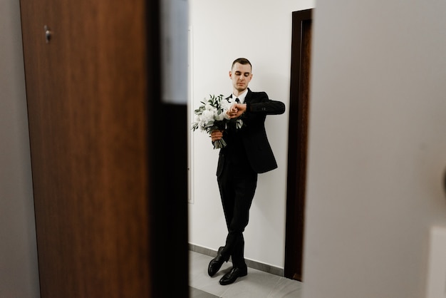 Der Bräutigam wartet auf die Braut, die unter der Tür steht und einen Hochzeitsstrauß aus Rosen in der Hand hält.