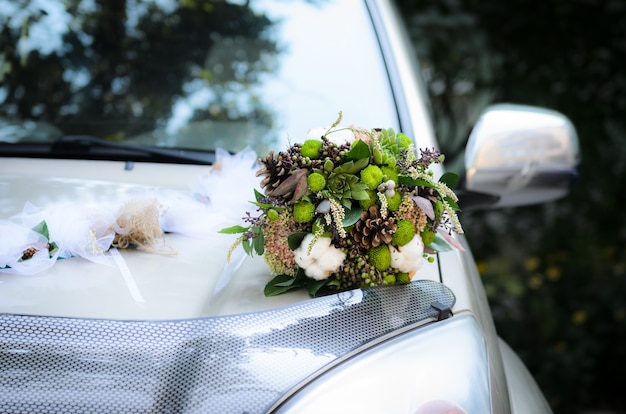 Der Brautstrauß aus Zapfen und Baumwolle auf der Motorhaube des Hochzeitsautos