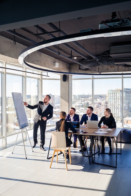 Der Chef steht mit Grafiken neben der Tafel, führt Statistiken vor, verschiedene Mitarbeiter nehmen an der Schulung teil, stellt die neuen Produkte des Unternehmens vor, berichtet über die Arbeitsergebnisse für Partner.