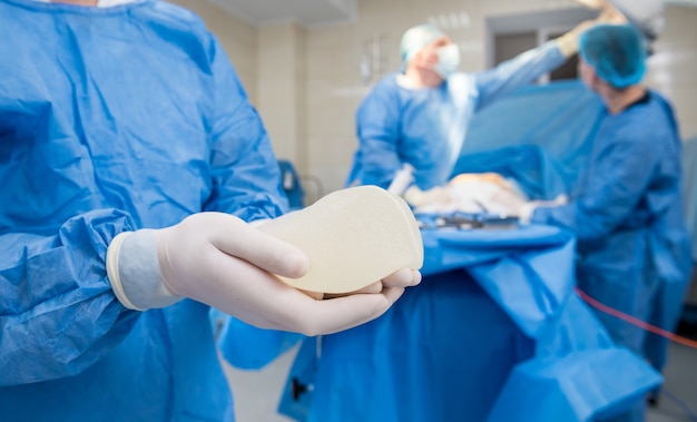Der Chirurg im Operationssaal hält ein steriles Brustsilikonimplantat in den Händen