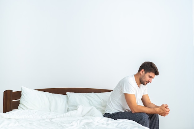 Der depressive Mann sitzt auf dem Bett auf dem weißen Hintergrund