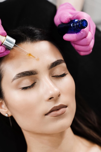 Foto der dermatologe trägt feuchtigkeitsspendendes serum auf das gesicht des models auf. der kosmetiker trägt hyaluronsäure oder serum aus der pipette auf das gesicht des geduldigen mädchens auf