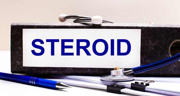 Der Desktop hat ein Stethoskop, einen blauen Stift und einen grauen Aktenordner mit dem Text STEROID Medical Concept