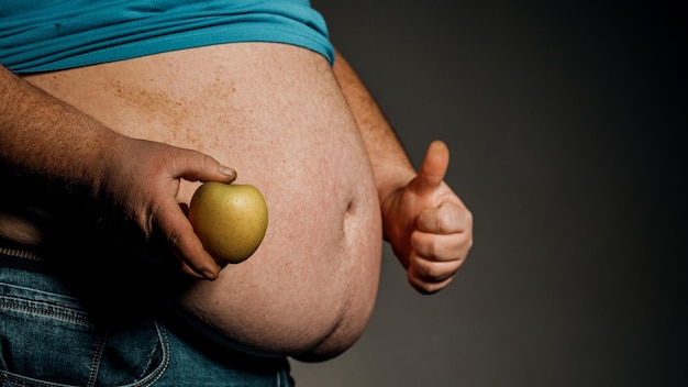 Der dicke Mann hält einen Apfel vor seinem nackten Bauch Das Konzept der Ernährung und gesunden Ernährung