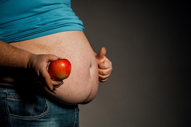 Der dicke Mann hält einen Apfel vor seinem nackten Bauch Das Konzept der Ernährung und gesunden Ernährung