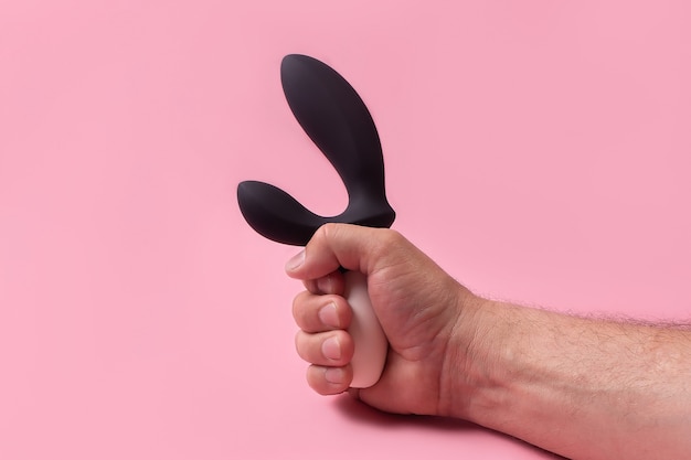 Der Dildo in der Hand auf einem rosa Hintergrund, Sexspielzeug