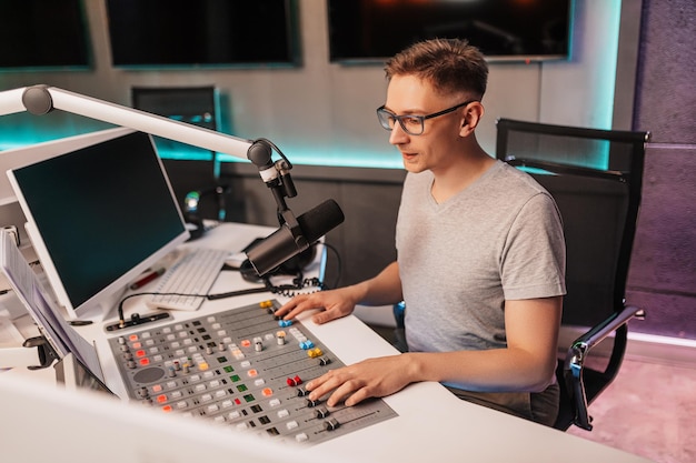 Der DJ moderiert das Programm und kommuniziert mit dem Publikum auf Sendung im Radiosender. Der Sprecher liest die Nachrichten. Ein männlicher Radiomoderator spricht in ein Mikrofon und nimmt einen Podcast auf