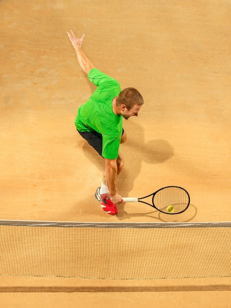 Der eine springende Spieler, kaukasischer fitter Mann, der Tennis auf dem irdenen Platz spielt