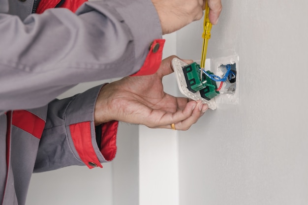 Der Elektriker prüft mit einem Schraubenzieher den Netzstecker an der Wand.