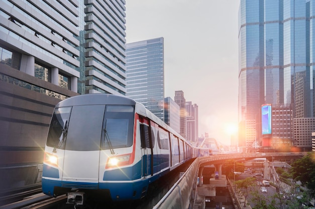 Der elektrische Zug BTS Skytrain fährt unterwegs mit Bürogebäuden im Hintergrund