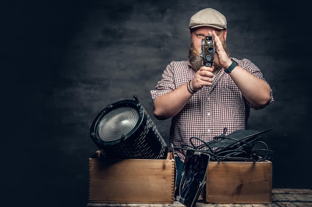 Der fette, bärtige Hipster-Mann hält eine alte 8-mm-Videokamera und bunte Laibungslampen.