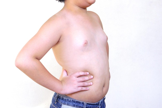 Der fette Junge trägt Jeans, die mit in die Seite gestemmten Armen auf weißem Hintergrund stehen. Gesundheits- und Bewegungskonzept.