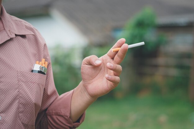 Der Finger eines Rauchers hält eine Zigarette auf der linken Seite, verschwommener Hintergrund, Süchtiger und Gesundheitsproblem, Lungenproblem, Konzept, Kopierraum für individuellen Text, der für nicht jugendfreie Inhalte verwendet wird