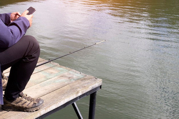 Der Fischer sitzt auf dem Pier und schaut auf das Telefon.