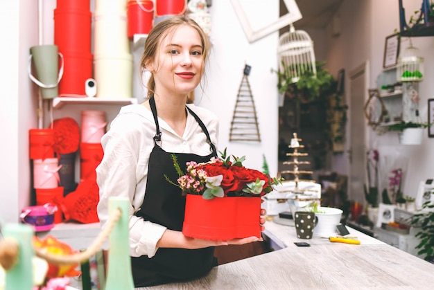 Der Florist der jungen Frau in der schwarzen Schürze hält in den Händen Hutschachtel mit Blumen