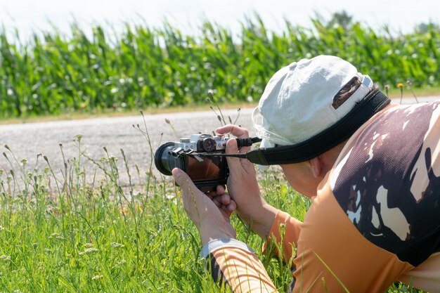 Der Fotograf liegt auf dem Boden und hält eine Kamera Ein junger Fotograf in der Natur in einer weißen Kappe Eine moderne Kamera in den Händen eines unerfahrenen Fotografen