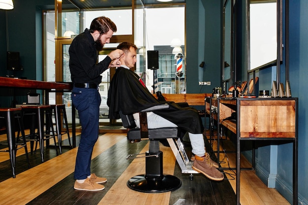 Der Friseur im schwarzen Hemd, der gerade einen Kunden im Friseursalon zerschneidet