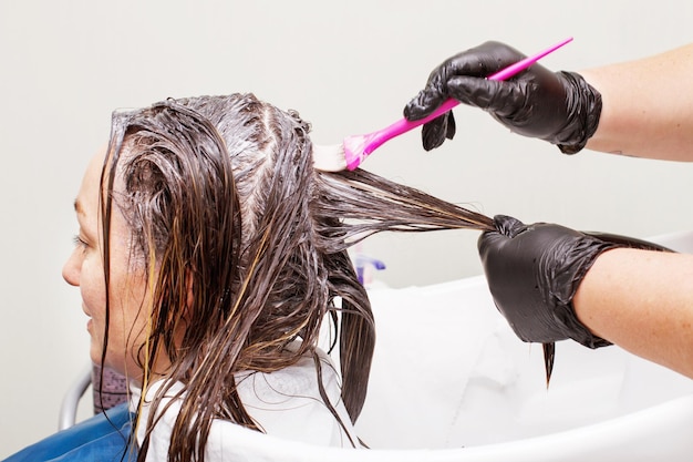 Der Friseur in schwarzen Handschuhen malt einer brünetten Frau im Schönheitssalon nah die Haare