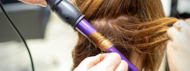 Der friseur macht mit dem lockenstab im friseursalon aus nächster nähe locken aus langen braunen haaren