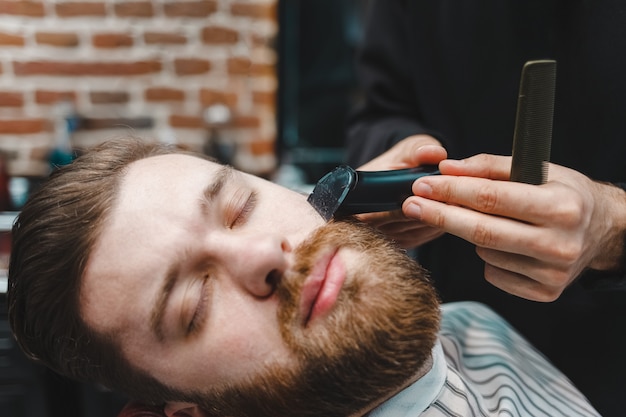 Der Friseur schneidet dem Kunden mit einem elektrischen Trimmer den Bart
