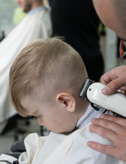 Der Friseur schneidet einem kleinen blonden Jungen im Friseurladen die Haare