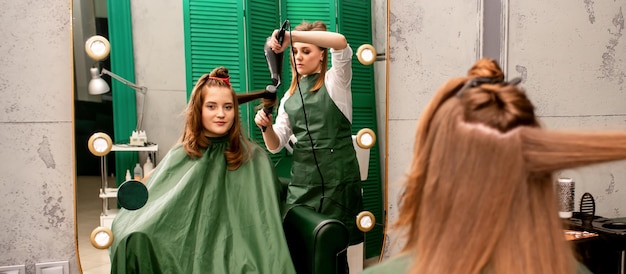 Der Friseur trocknet lange braune Haare mit Haartrockner und Rundbürste in einem Schönheitssalon