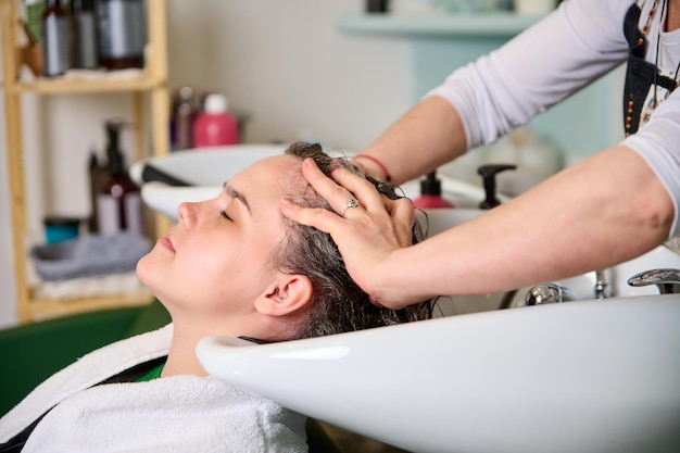 Der Friseur wäscht den Kopf eines brünetten Mädchens mit Shampoo im Schönheitssalon