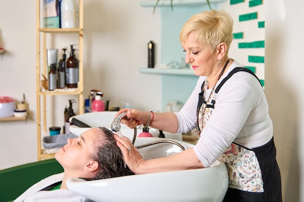 Der Friseur wäscht den Kopf eines brünetten Mädchens mit Shampoo im Schönheitssalon