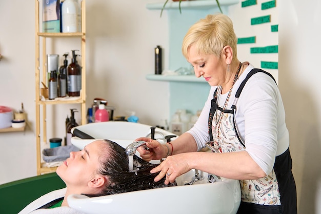 Der Friseur wäscht den Kopf eines brünetten Mädchens mit Shampoo im Schönheitssalon