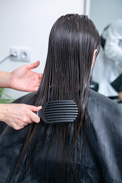 Der Friseur wendet eine Haarmaske auf glattes schwarzes Haar an.