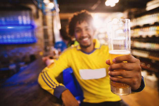 Der fröhliche Fußballfan im Trikot begrüßt den Sieg seines Vereins mit einem halben Liter Bier.