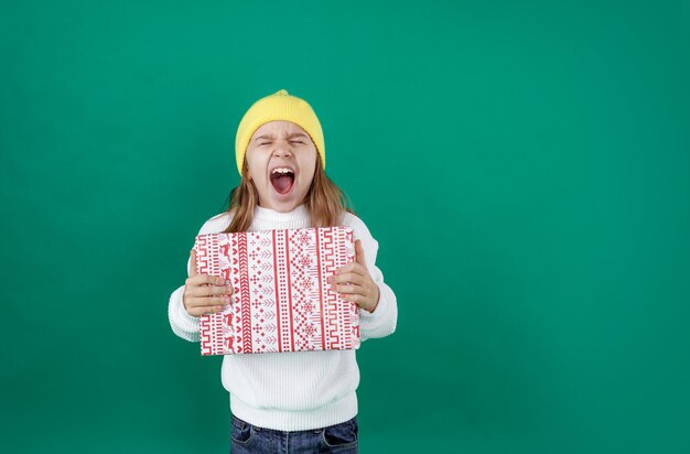 Der fröhliche Junge schreit laut, macht den Mund weit auf und umklammert eine Schachtel mit einem Neujahrsgeschenk. Glück und Freude der Kinder
