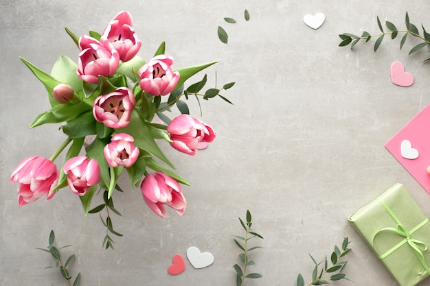 Der Frühling lag flach mit rosa Tulpen, Eukalyptusblättern und Geschenkboxen auf Steinoberfläche