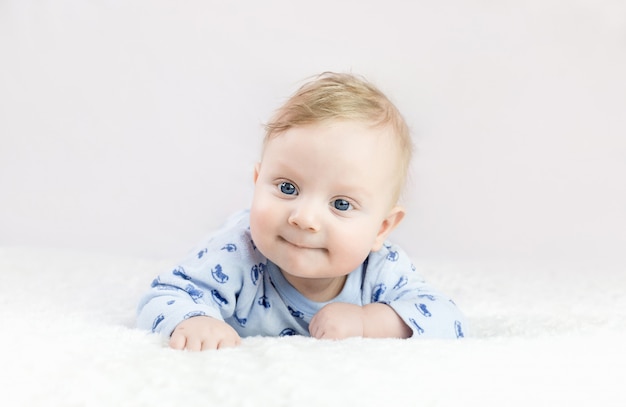 Der fünf Monate alte blonde Junge mit den blauen Augen liegt auf dem Bauch
