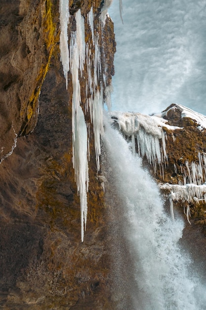 Der gefrorene Kvernufoss-Wasserfall mit Schnee und bläulichen Stalagmiten, von denen Wasser herabfällt