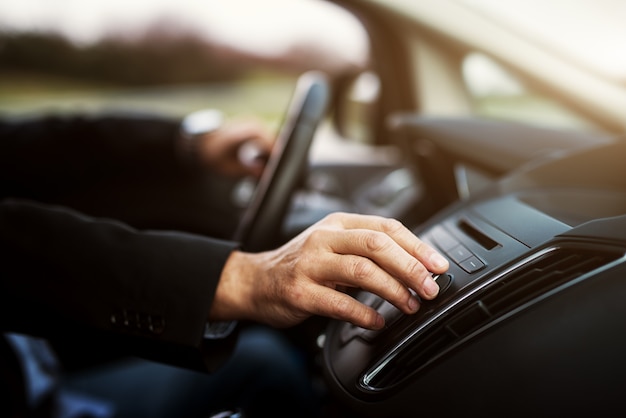 Der Geschäftsmann im Anzug stellt die Lautstärke seiner Stereoanlage ein, während er ein Auto fährt.