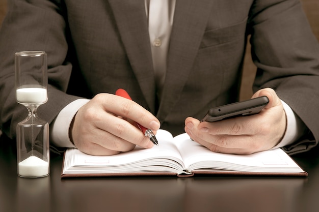 Der Geschäftsmann im Büro arbeitet mit einem Mobiltelefon auf einer Sanduhr. Geschäft und erfolgreiches Ziel