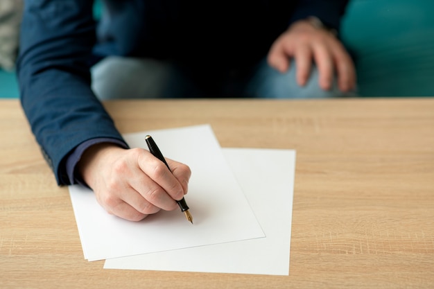 Der Geschäftsmann im Büro schreibt einen Brief oder unterschreibt ein Dokument auf einem weißen Blatt Papier mit einem Füllfederhalter mit Feder.